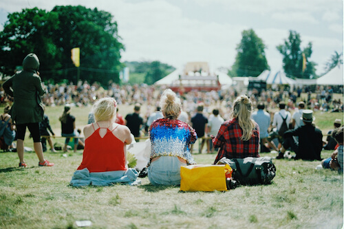 Three blonde girls sitting on grass at a music festival.